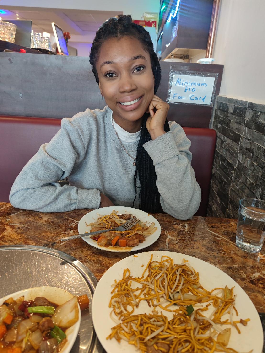A person smiling with three bowls of food and a glass of water on a table