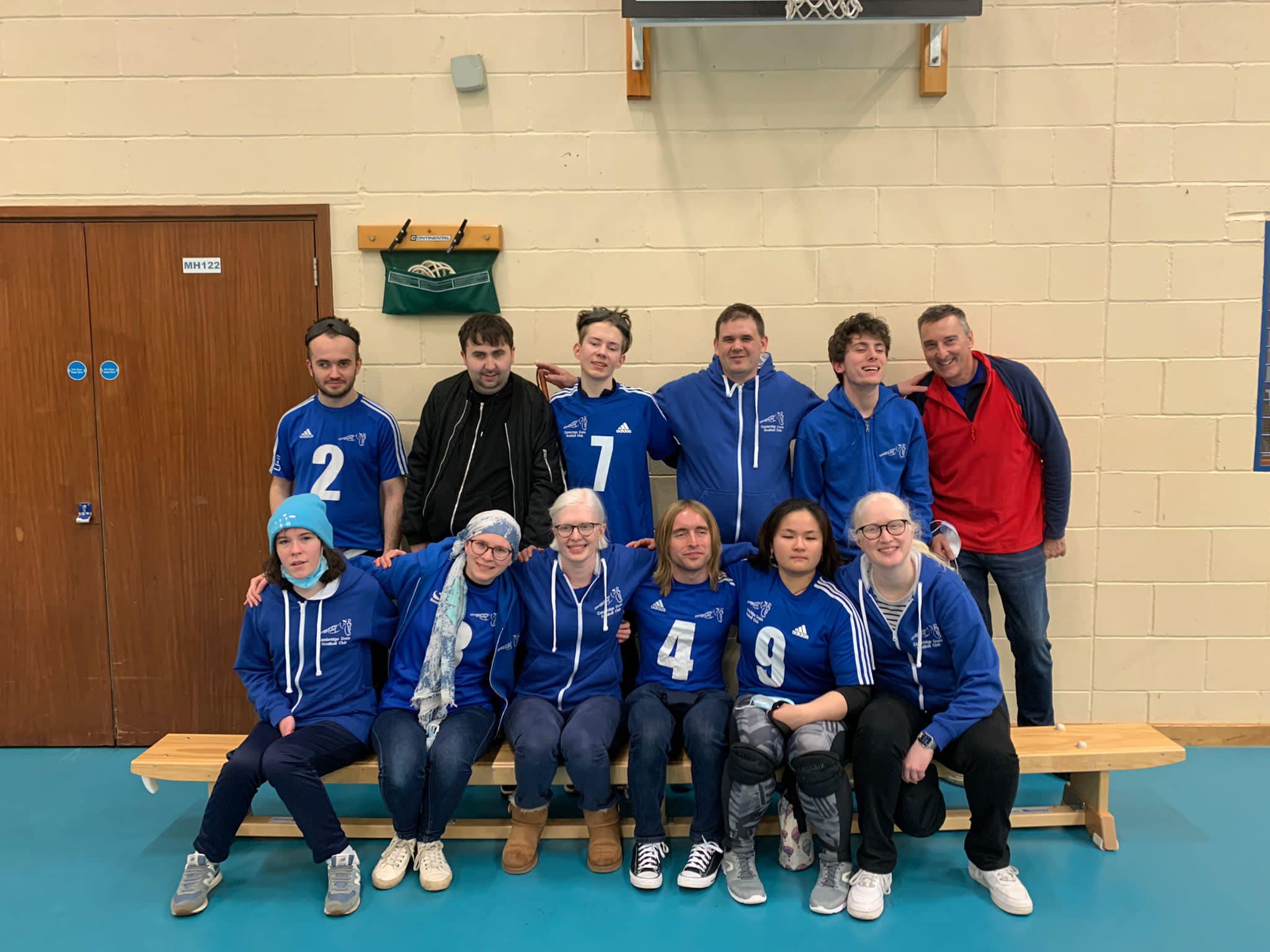 Two rows of six people in blue tracksuit tops posing for a photo