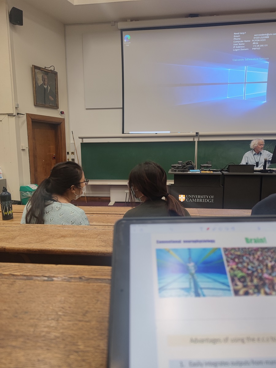 A laptop screen in a tiered lecture room, with a projector screen mounted on a wall