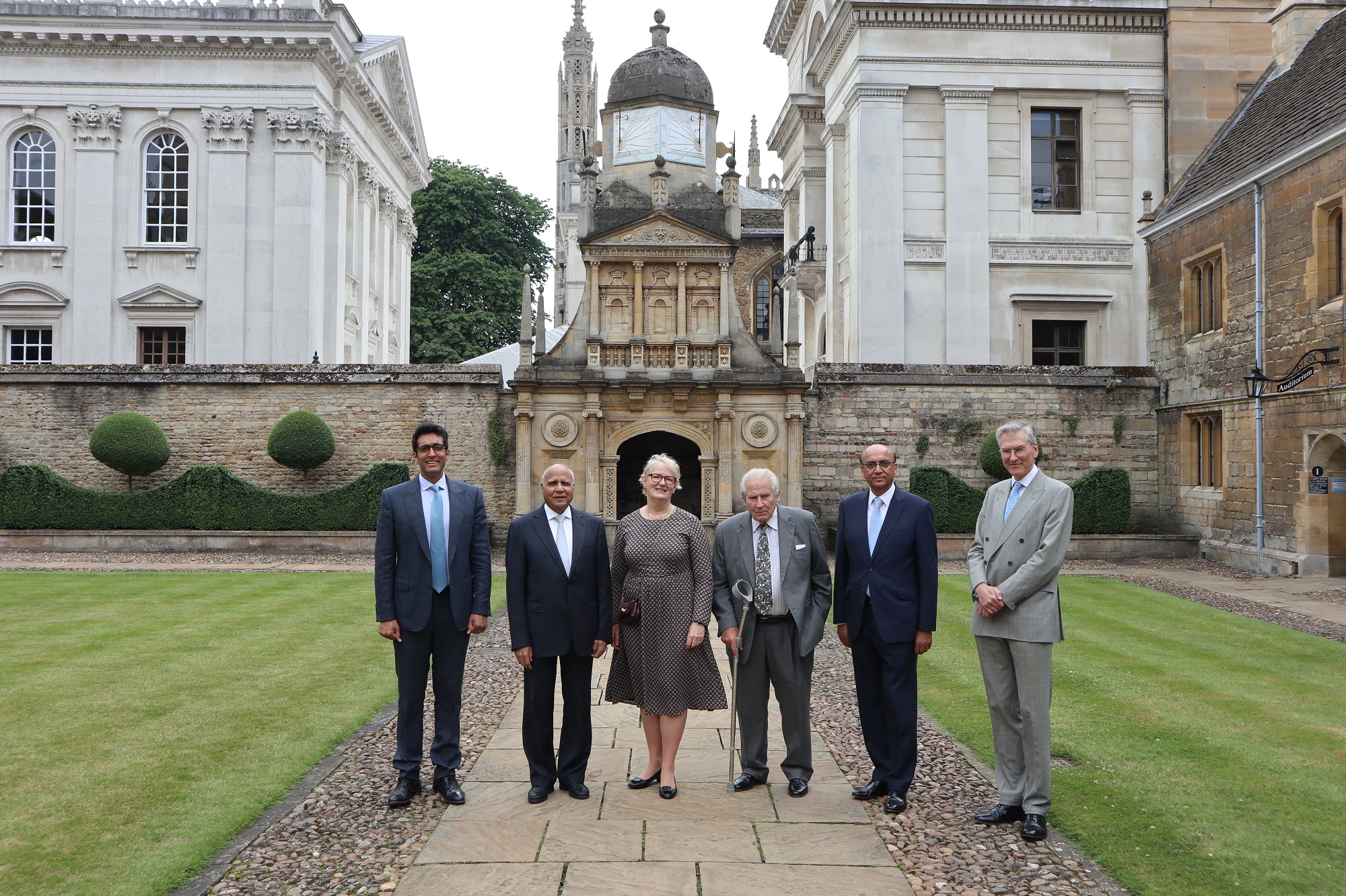 Haider Choudrey, Sir Anwar Pervez, Dr Pippa Rogerson, Sir Nicolas Barrington, Lord Zameer Choudrey, and Robert Gardiner standing in Caius Court in front of the Gate of Honour