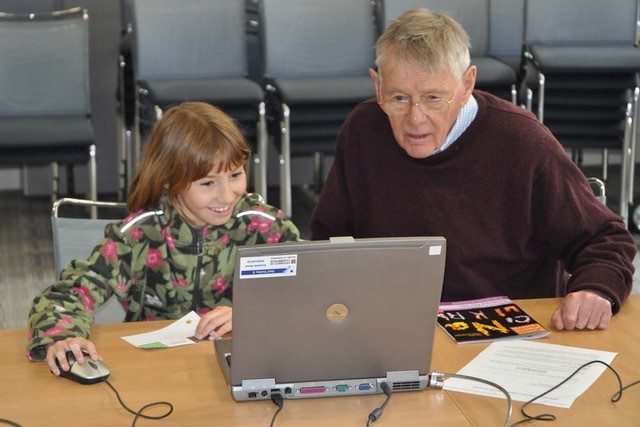 A child and a man work together on a laptop computer at a Cambridge outreach experiment