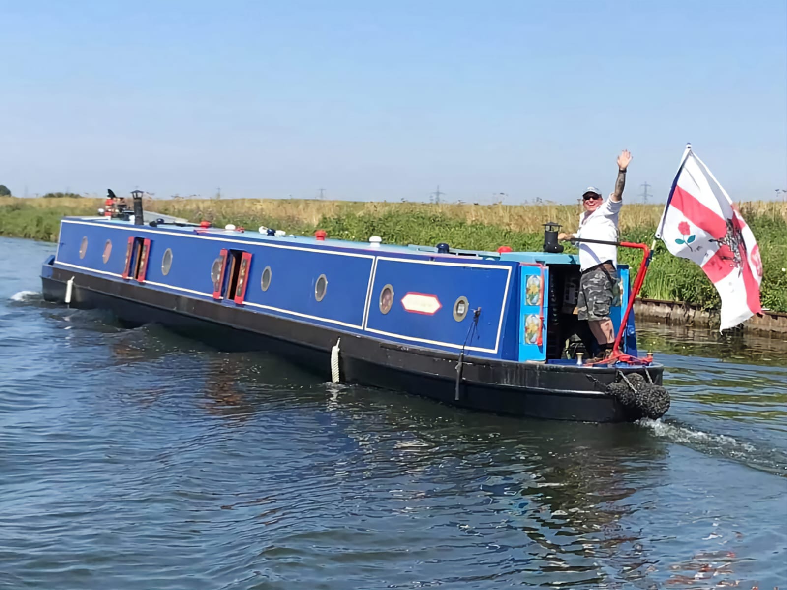 A man waving from the back of a narrowboat