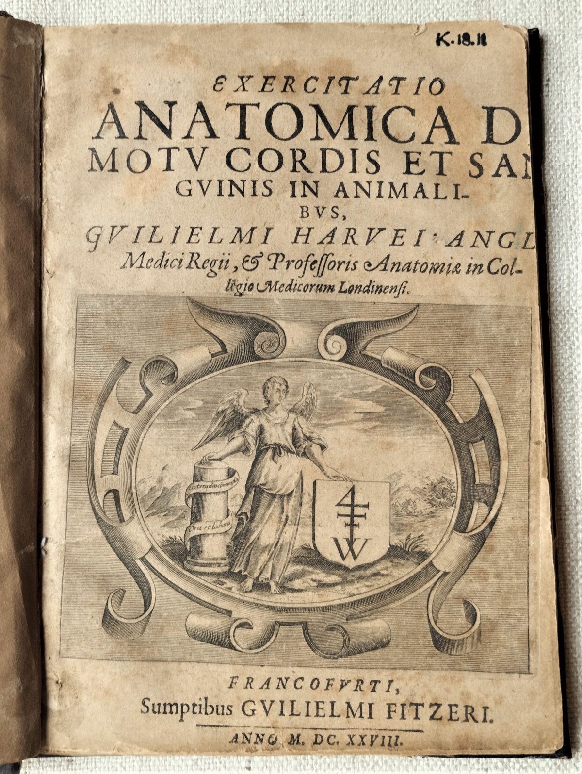 Ttile page of the book "Exercitatio anatomica de motu cordis et sanquinis in animalibus" by William Harvey (1628). It contains an engraved illustration of an angel showing a coat of arm and a column with a latin motto on it.