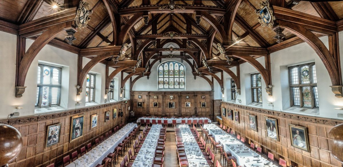 A large hall with four long banquet tables and a top table set for formal dining
