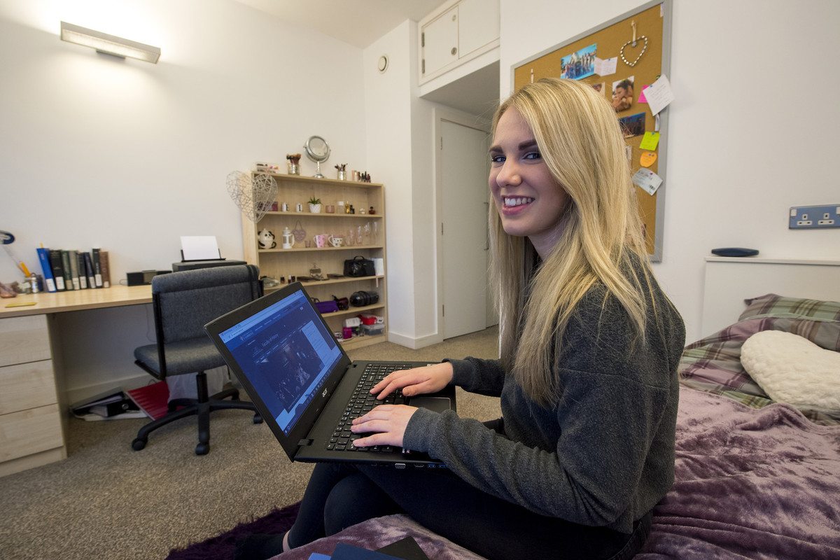 A woman sitting on a bed holding a laptop computer