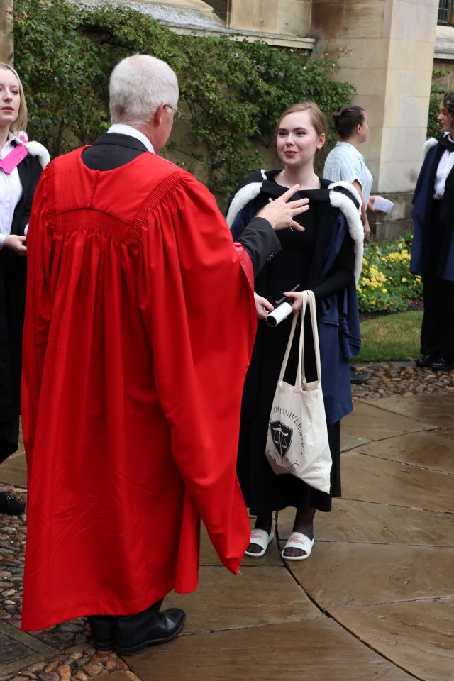 A student in a graduation gown with a bag speaks to an academic in a red gown