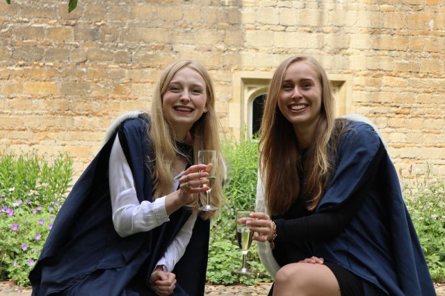Two female graduates celebrate with a glass of champagne