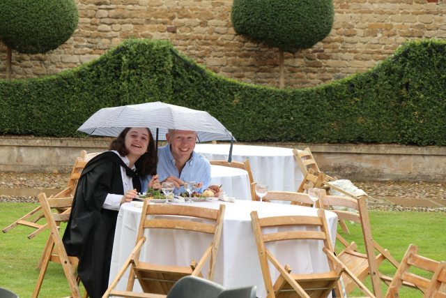 Two people huddled under an umbrella eating lunch